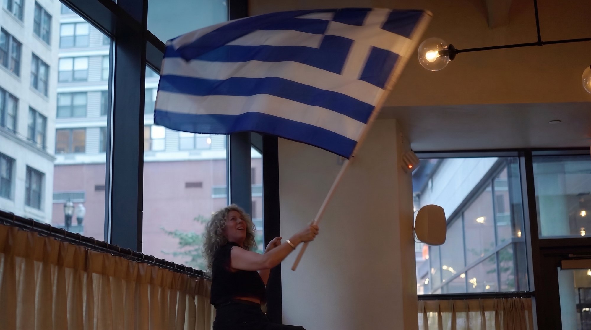 A guest waving the Greek flag as the room cheers during Greek Night at IKOS