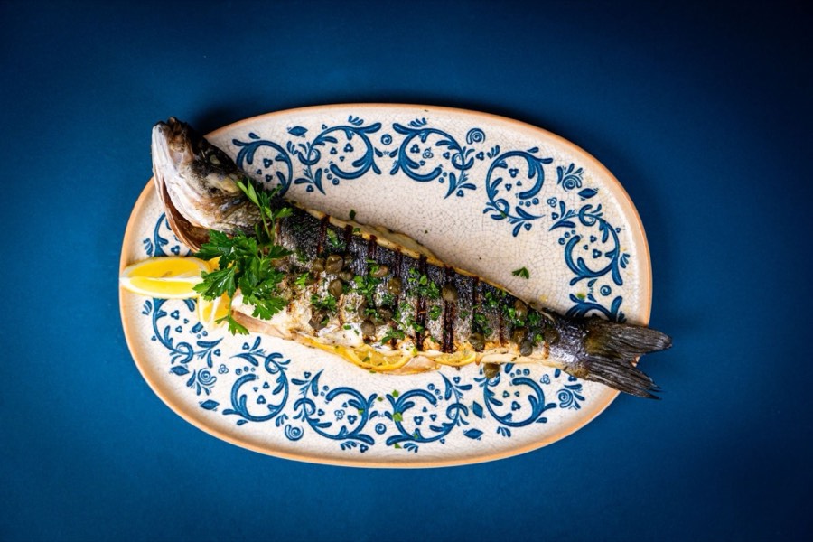 A whole grilled fish served on a blue Greek platter